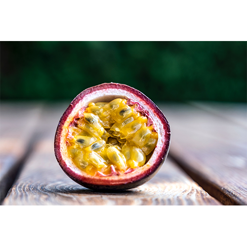 A cut passionfruit sitting on a wood desk with yellow inside and pink outside