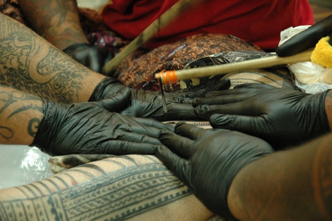 One artist dips the tip of a wooden instrument in black ink and methodically taps it into the wearer's body while two others stretch his skin as tight as they can