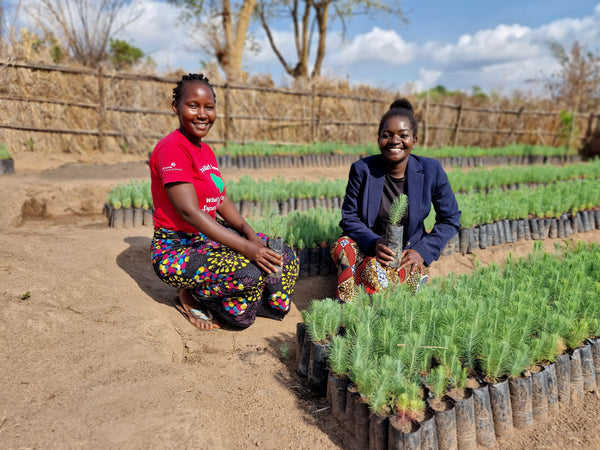 Two women from the Ripple Africa team smiling crouched amongst saplings