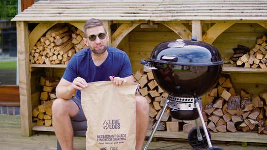 Paul from Love Logs sat next to a kettle BBQ holding a bag of charcoal
