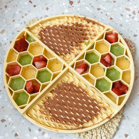 Pastel yellow lick mat with various fruits and vegetables