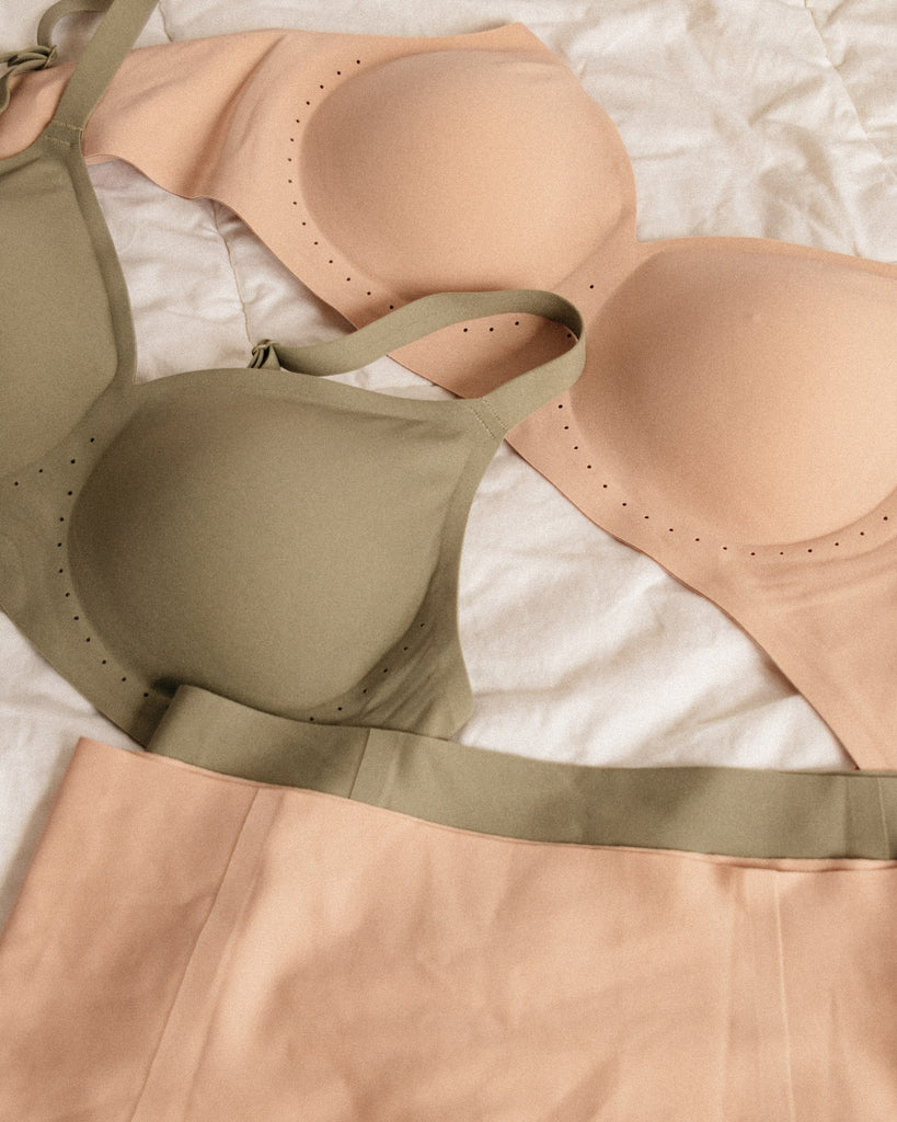 A light pink and a light green bra are laid out on a bed, along with the matching underwear.