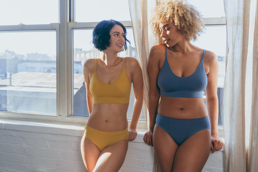 Our bralette set in Seals Blue and Golden Turmeric on 2 models, Morgan and Adrienne, leaning against the wall.