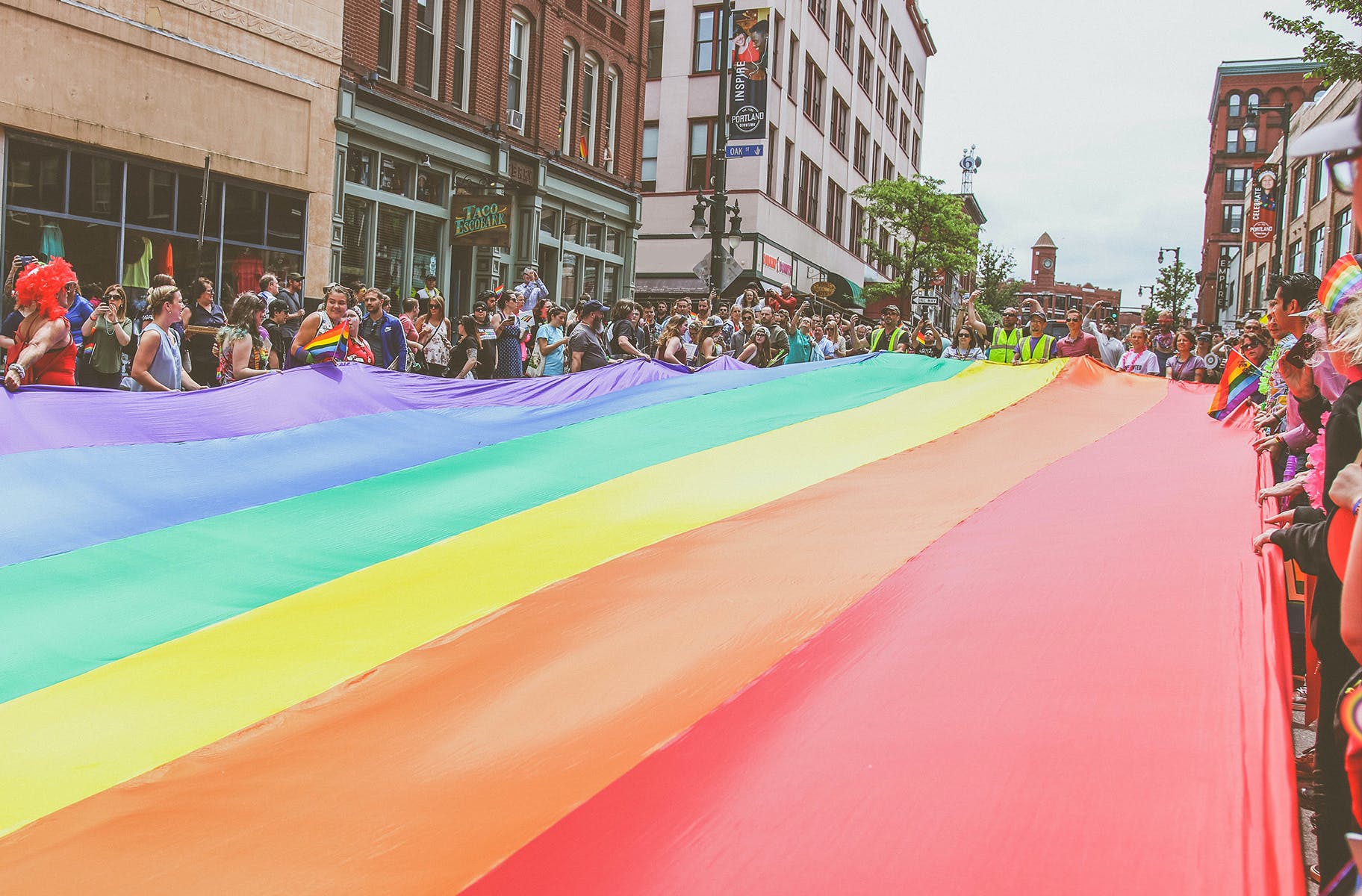 A big group of people holding a large pride flag in downtown San Francisco. 