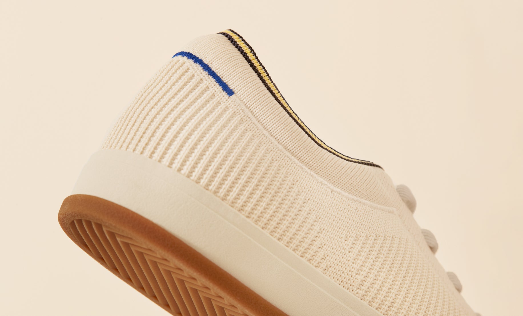 Close up of the heel area of The Lace Up in Vanilla, showing the Rothy’s blue halo detail, plush ankle collar and gum outsoles. 