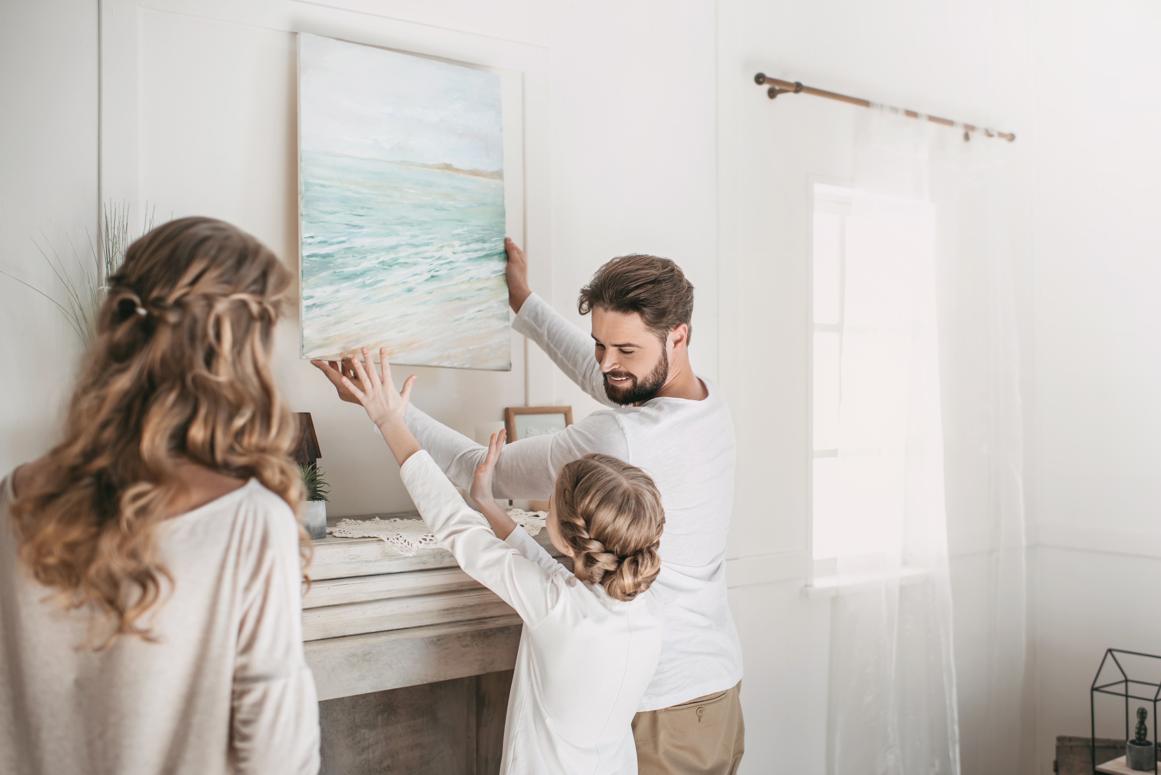 A family hanging a piece of neutral artwork in their living room.