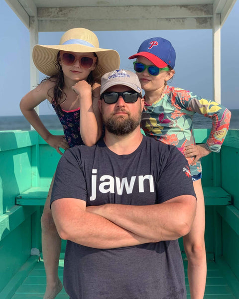 Man on beach wearing a Phillygoat Jawn t-shirt with his two kids posing behind him