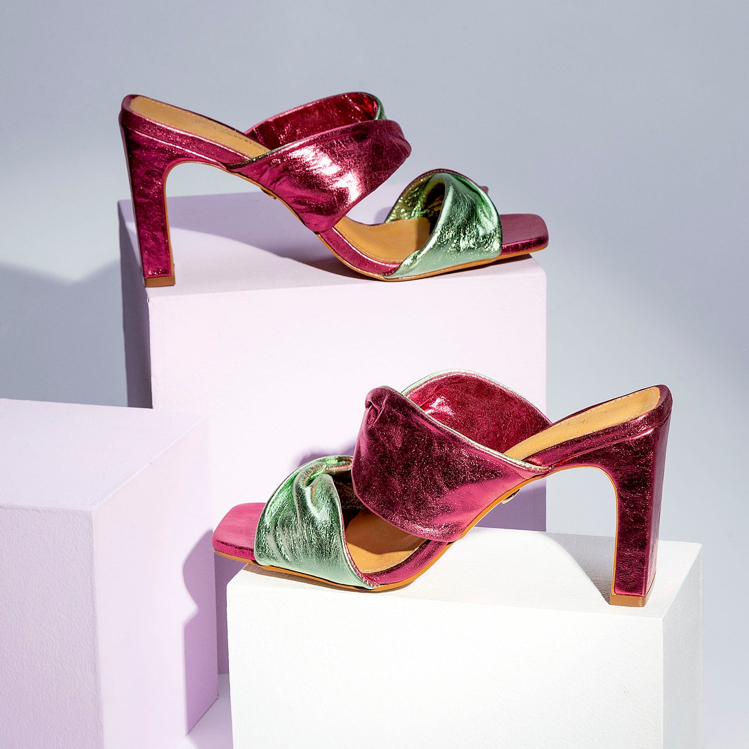 A pair of pink and green women's block heels sandals sitting on top of a white block.