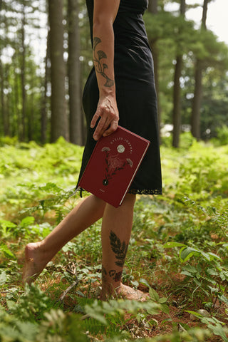 Rachael is in the woods walking and holding a Cycles journal.