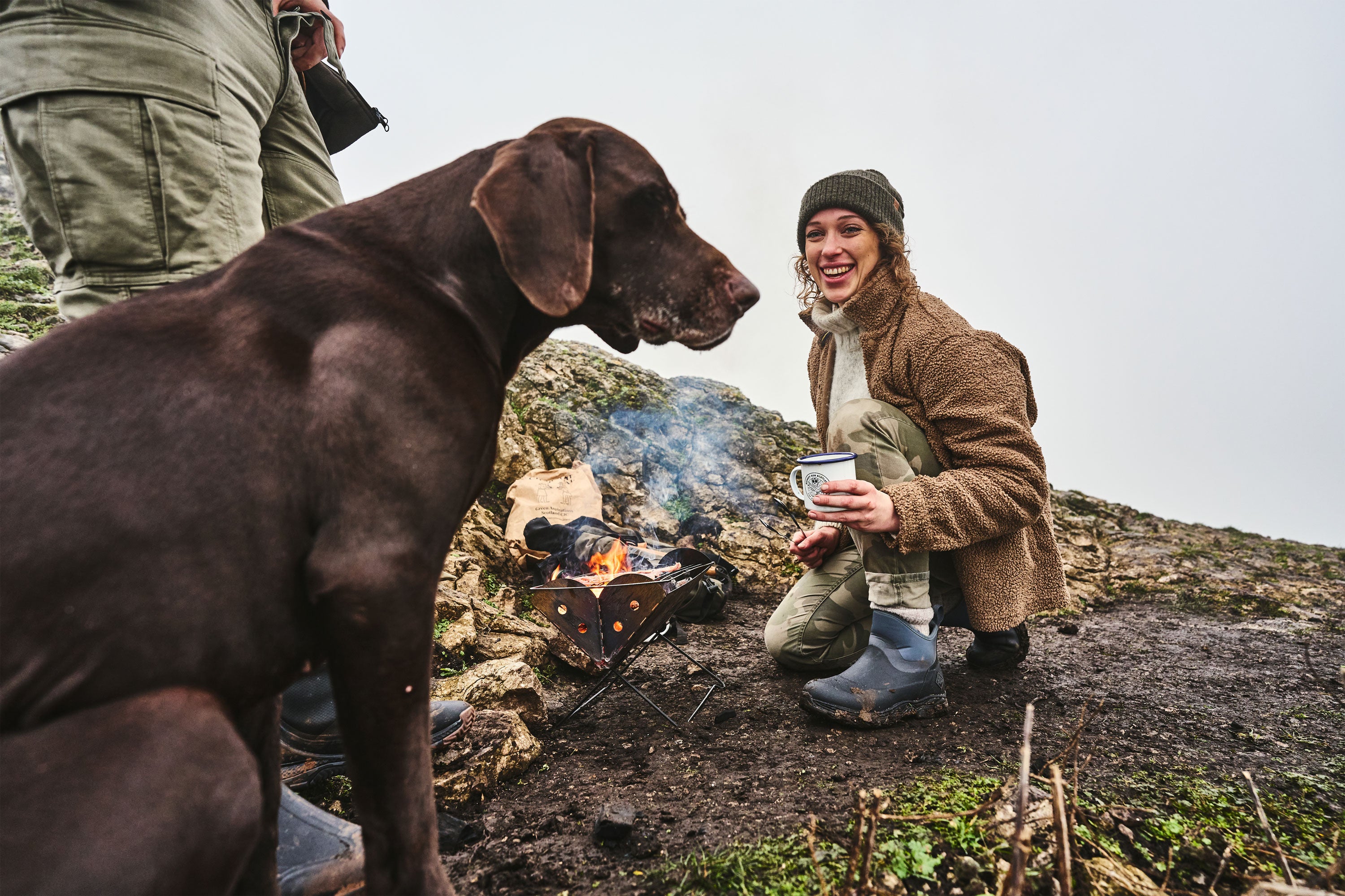 Lucy Pattinson kauert neben ihrem Hund und kocht draußen Essen