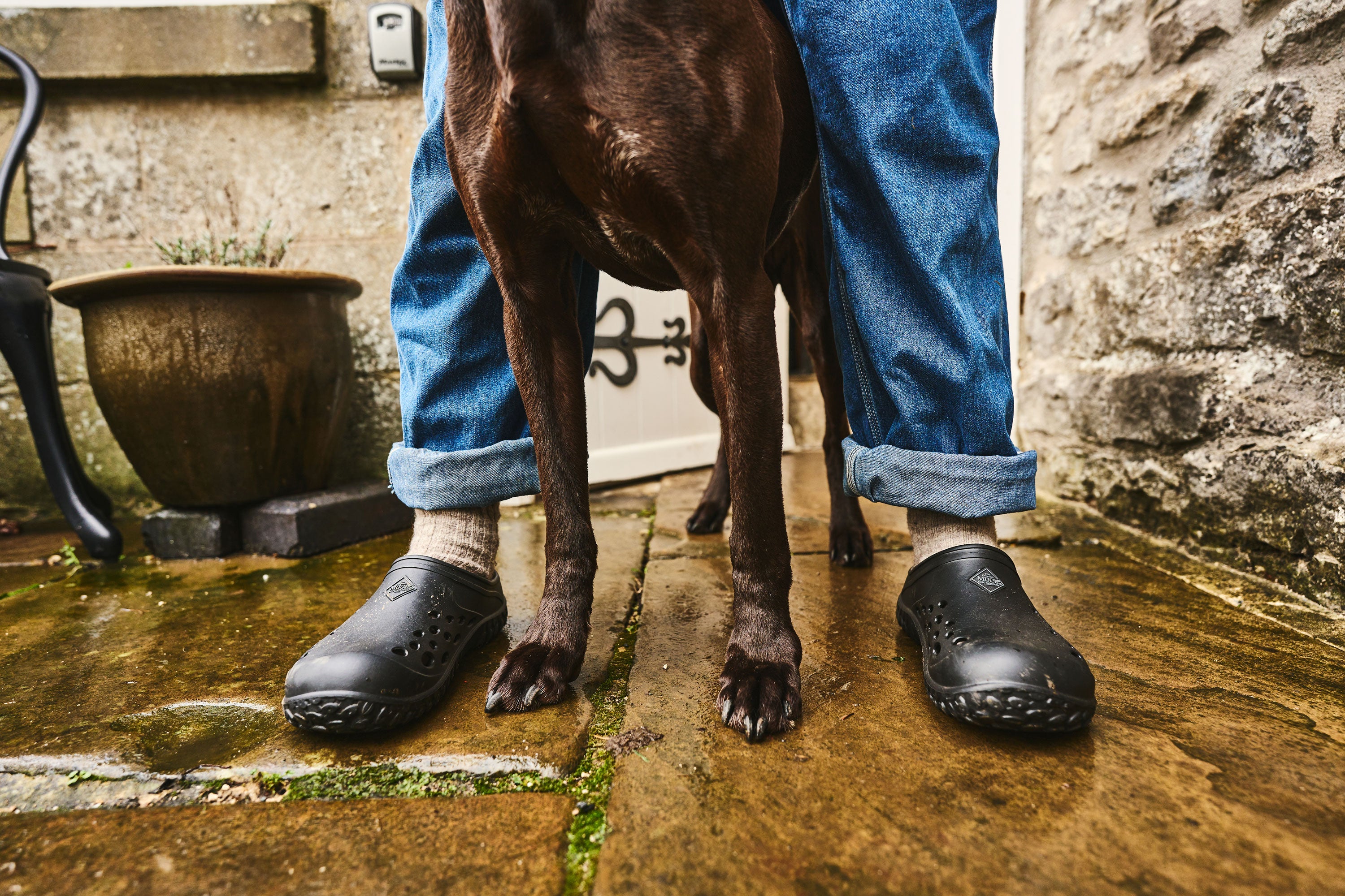 Person steht mit einem Hund zwischen den Beinen und trägt ein Paar Muck Boots Muckster Lite Clogs