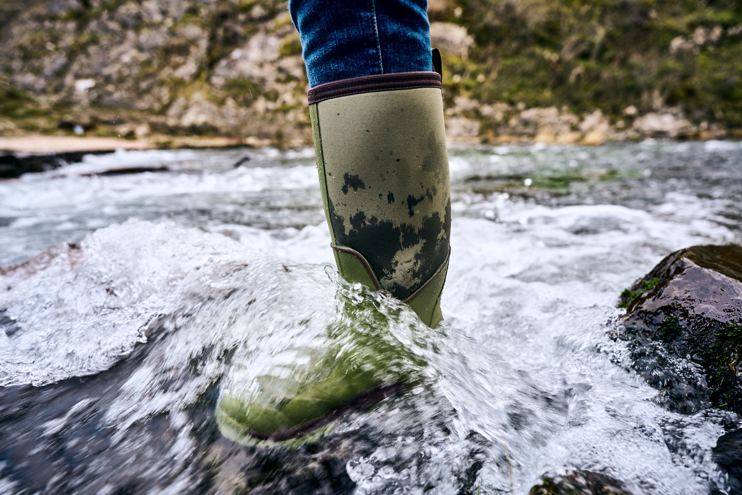 Person's foot, wearing a Muck Boots Calder wellington in a rocky stream