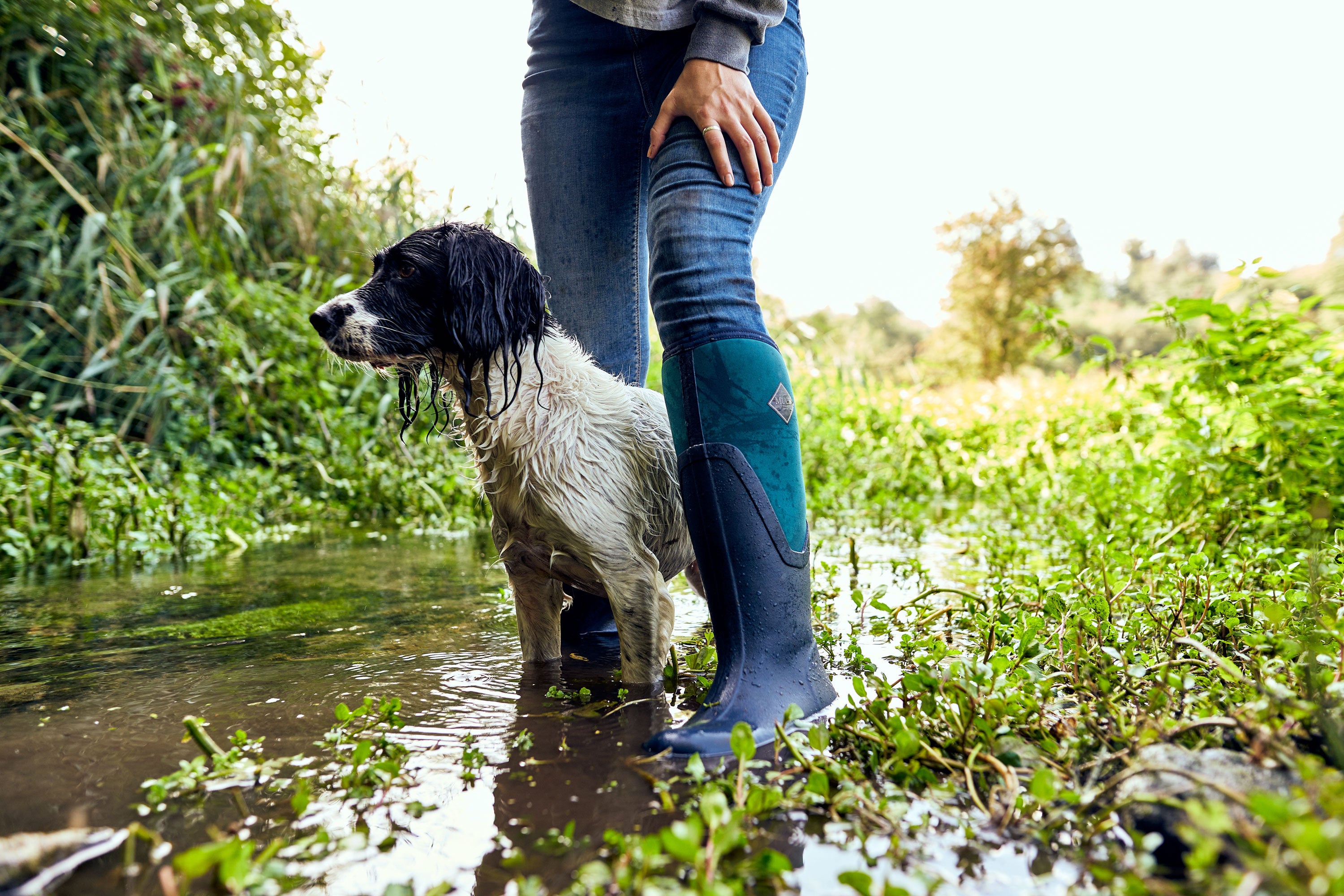 Person stood in a stream with a dog, wearing a pair of Muck Boots Arctic Sport II Wellingtons