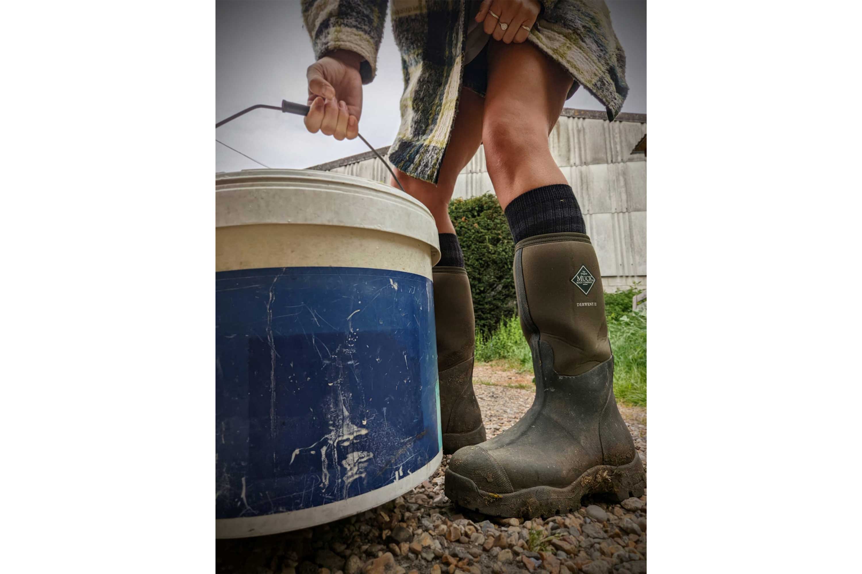 Close up of Zoë Colville holding a blue bucket and wearing a pair of Muck Boots Derwent II Wellingtons