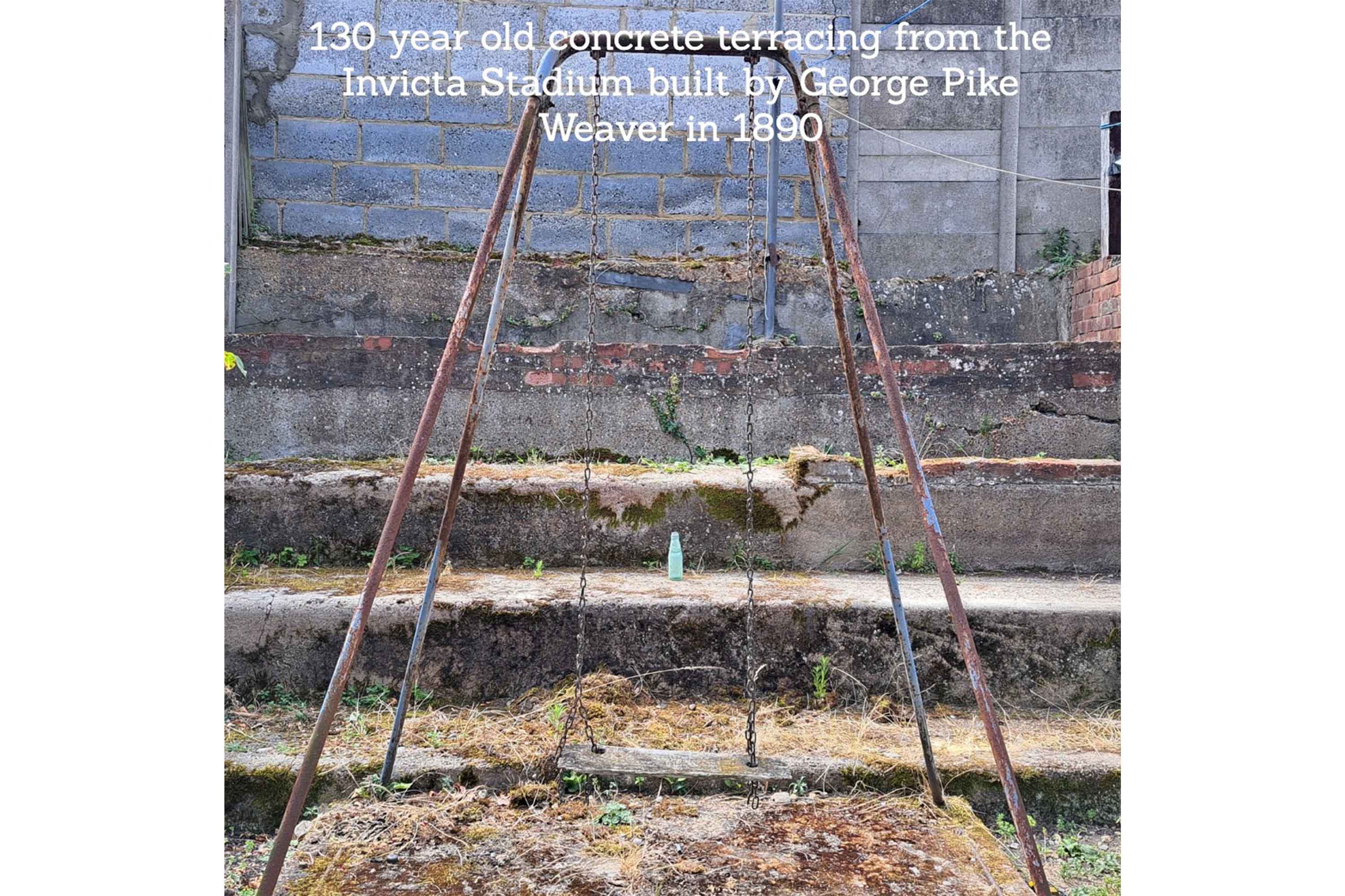 A 19th Century G.P.WEAVER OF PLUMSTEAD mineral water bottle sat on a terrace step of the old Invicta stadium with a swing in the foreground and text at the top that reads '130 year old concrete terracing from the Invicta Stadium built by George Pike Weaver in 1890