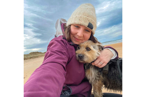 Emily wearing a pink jacket and beanie hat on a beach with her dog Murphy