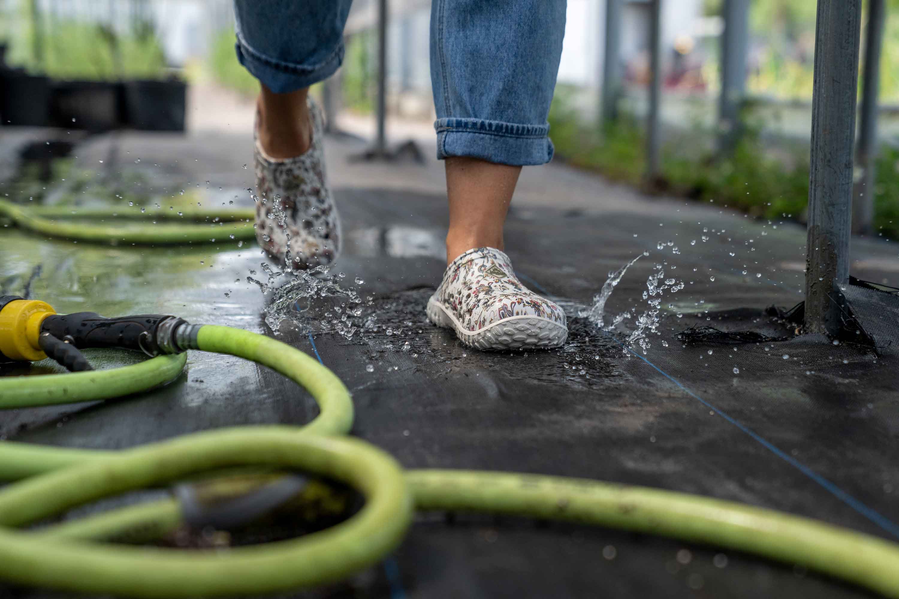 Eine Person trägt ein Paar Muckster Lite Clogs für Damen und läuft über einen nassen Holzboden auf dem ein Schlauch liegt