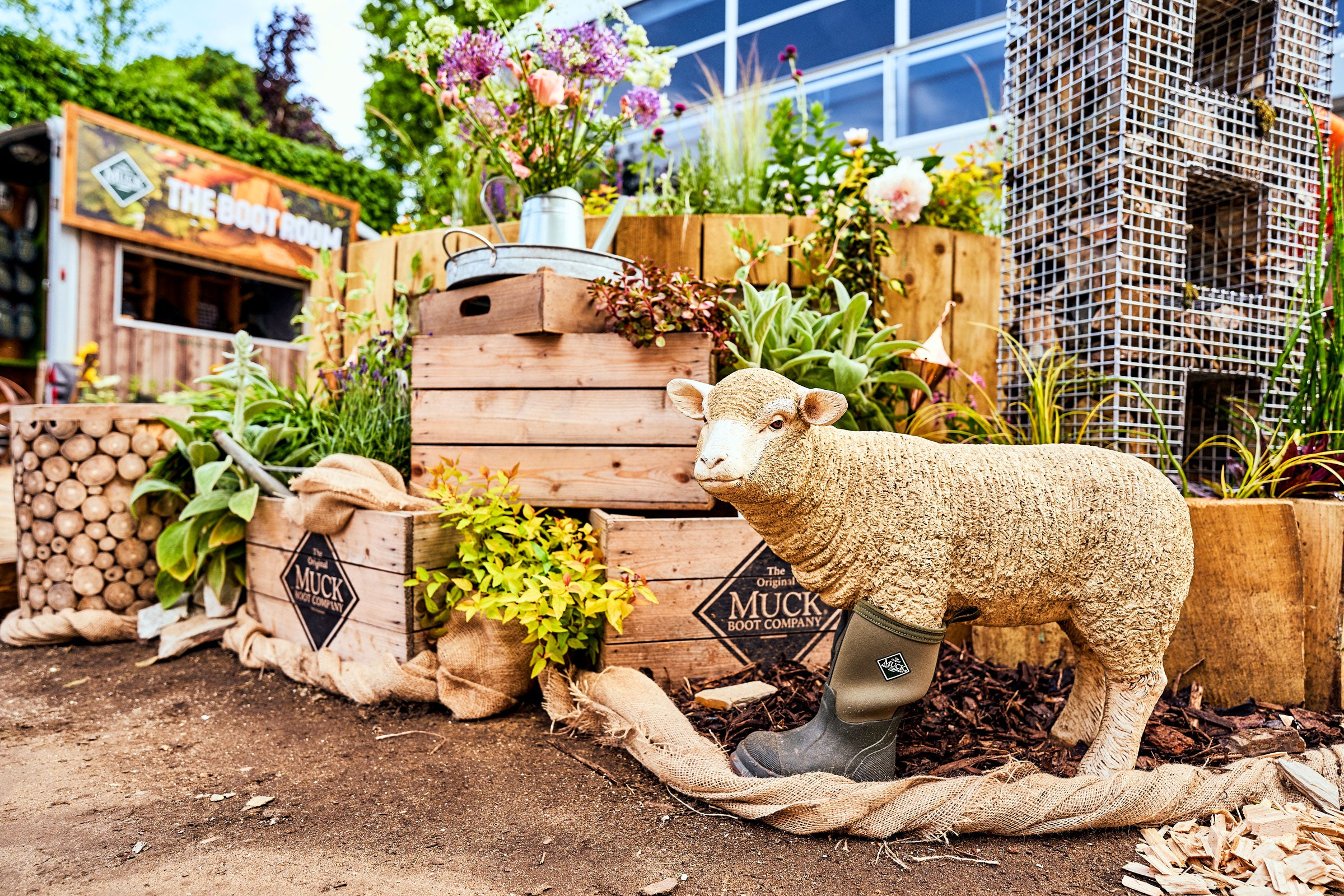 Model sheep wearing a Muck Boots welly in front of crates and flowers