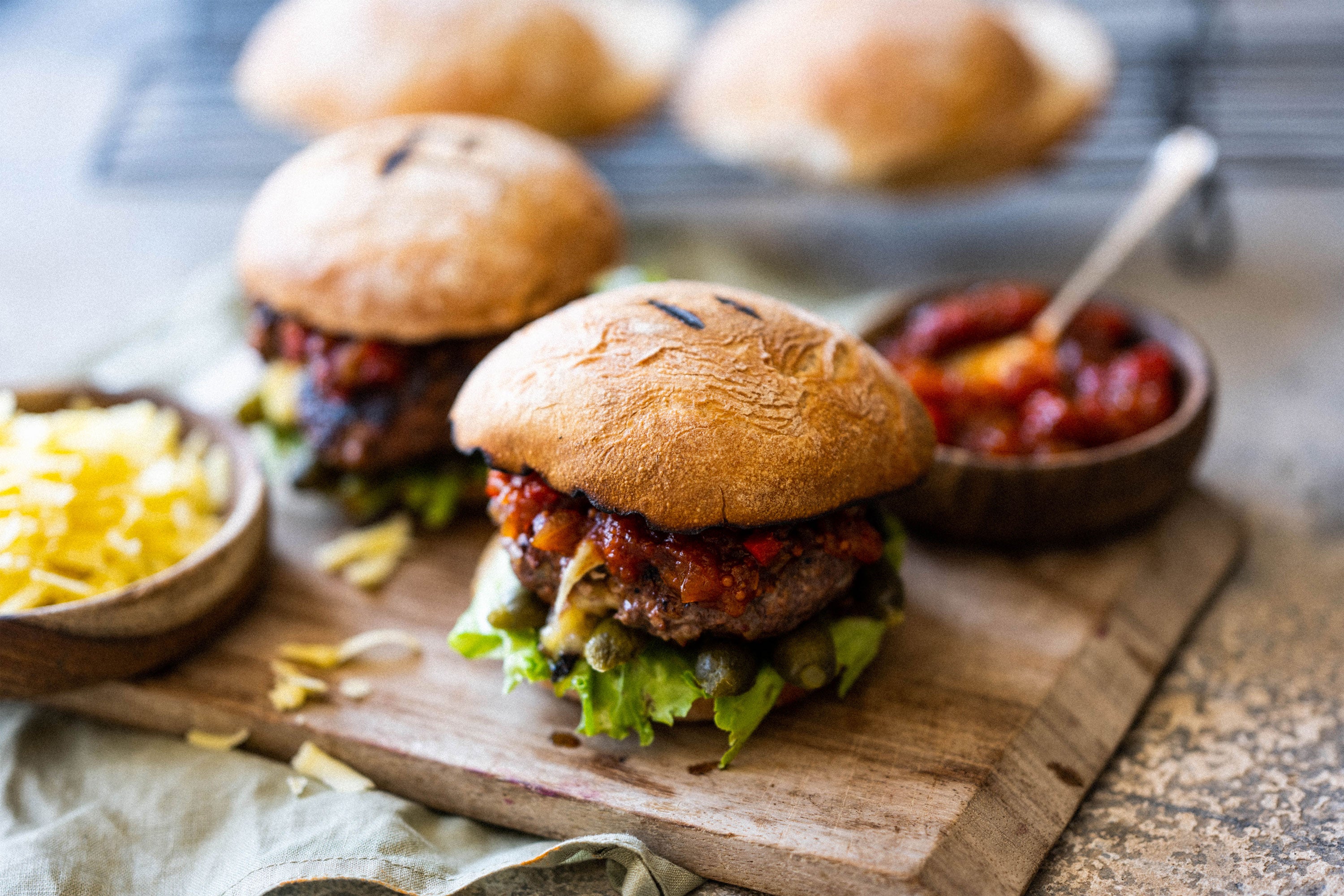 Finished burgers served on a wooden board with tomato relish and cornichons