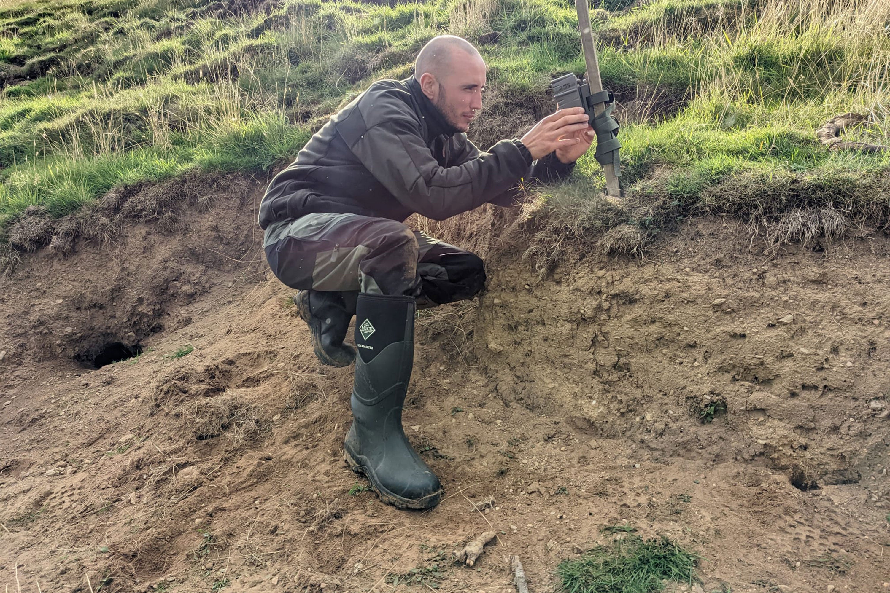 A Saving Wildcats volunteer replacing batteries on a trail camera wearing a pair of Muck Boots