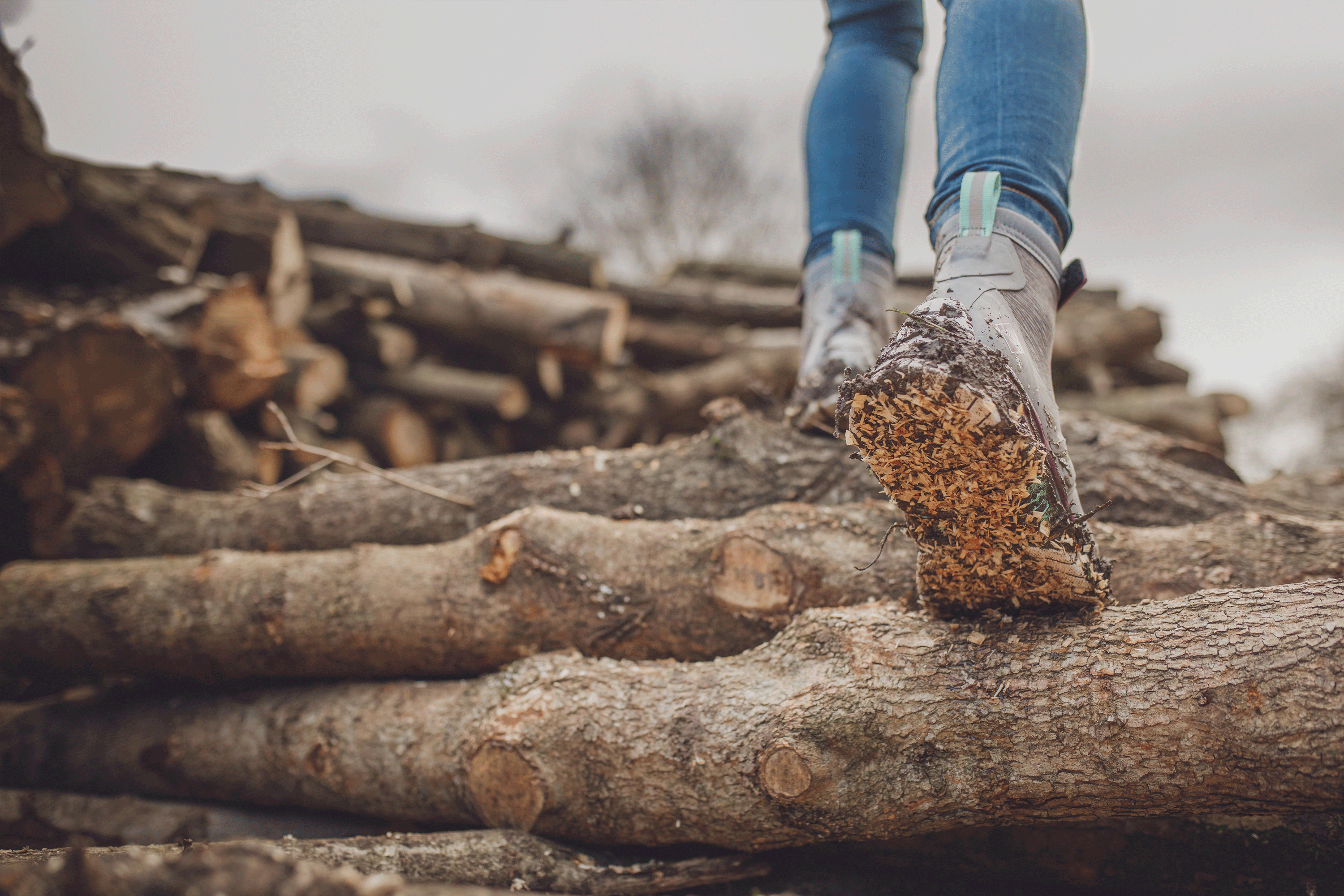 Woman walking up a pile of logs, showing the outsole of her right boot.