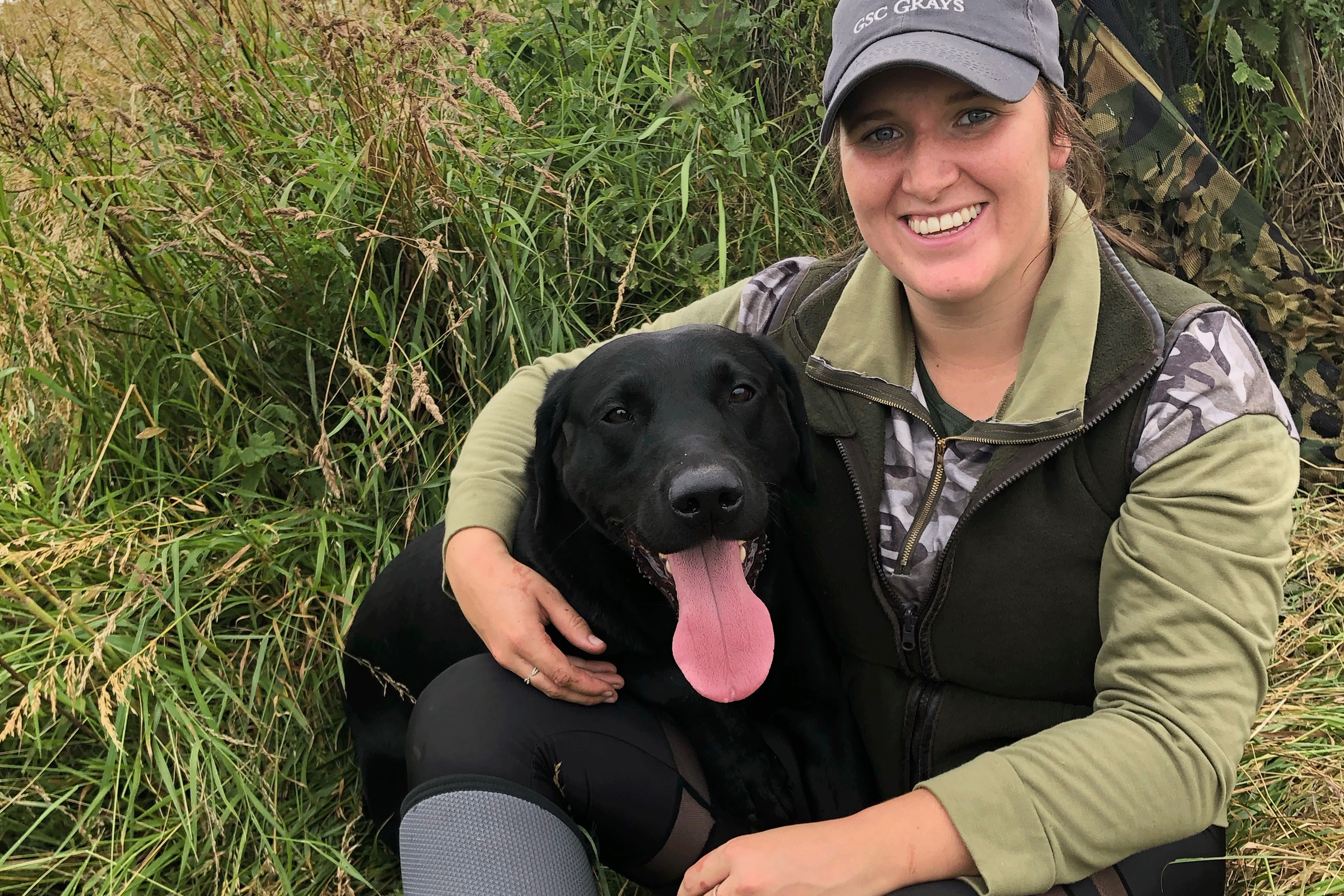 Woman in green countryside attire hugging her dog.