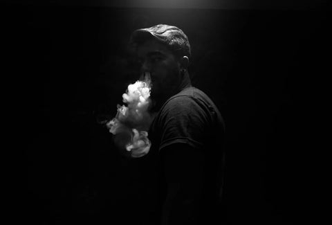 A man exhaling smoke on a black background.