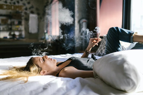 blonde women smoking on a bed with white sheets