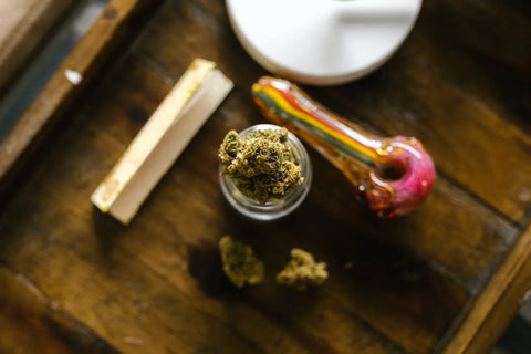 colorful glass pipe with rolling papers and weed on a wooden table