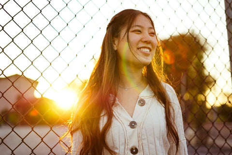 A woman smiling in front of a fence during the golden hour.