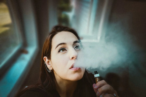 A woman holding and smoking on a black vape.