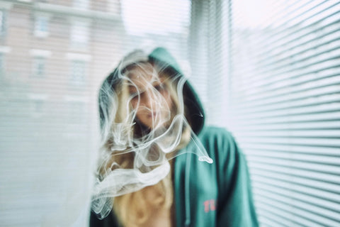 Blonde girl with a green hoodie vaping in the corner of her room