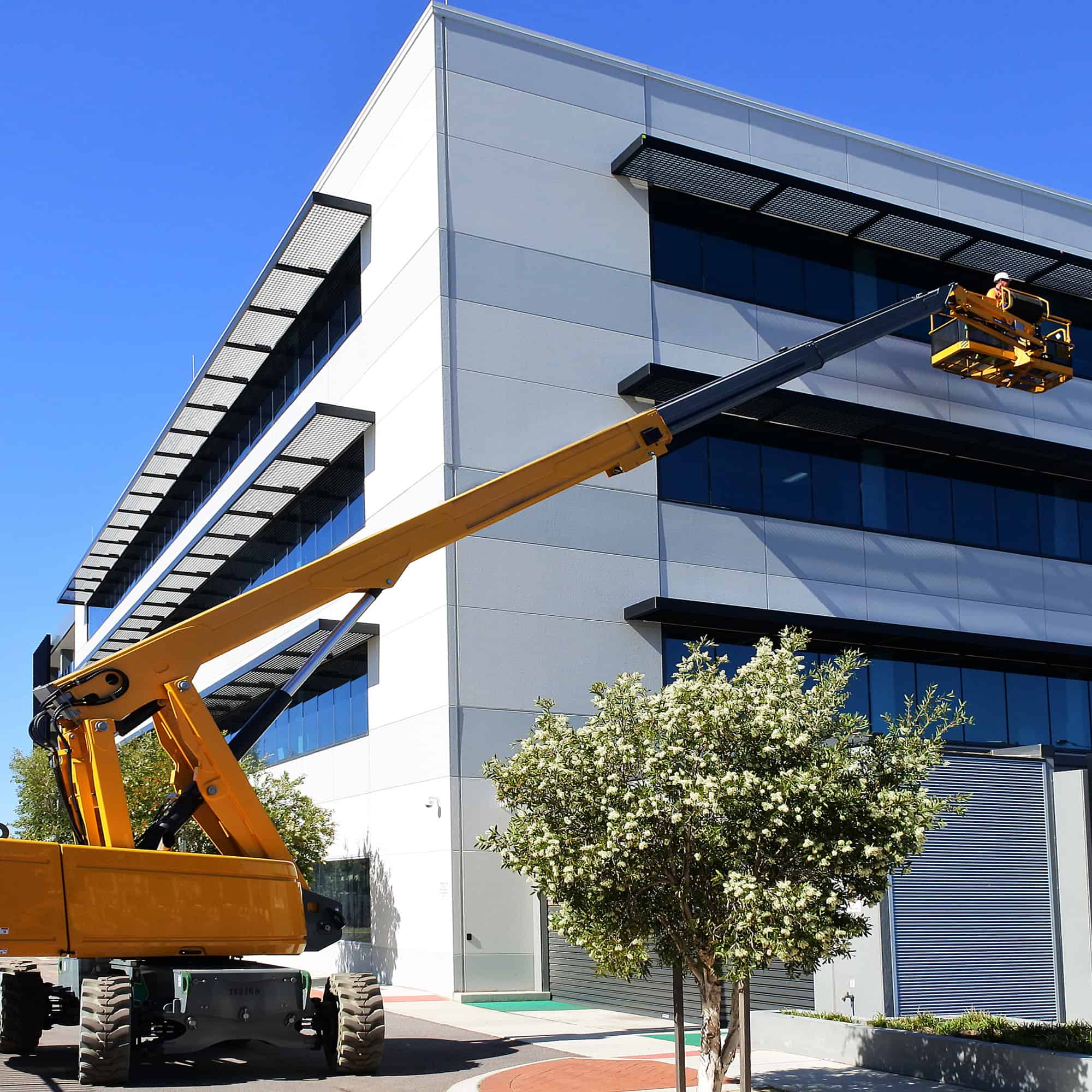 A fully extended boom lift holding a construction worker next to the top story window of an office building