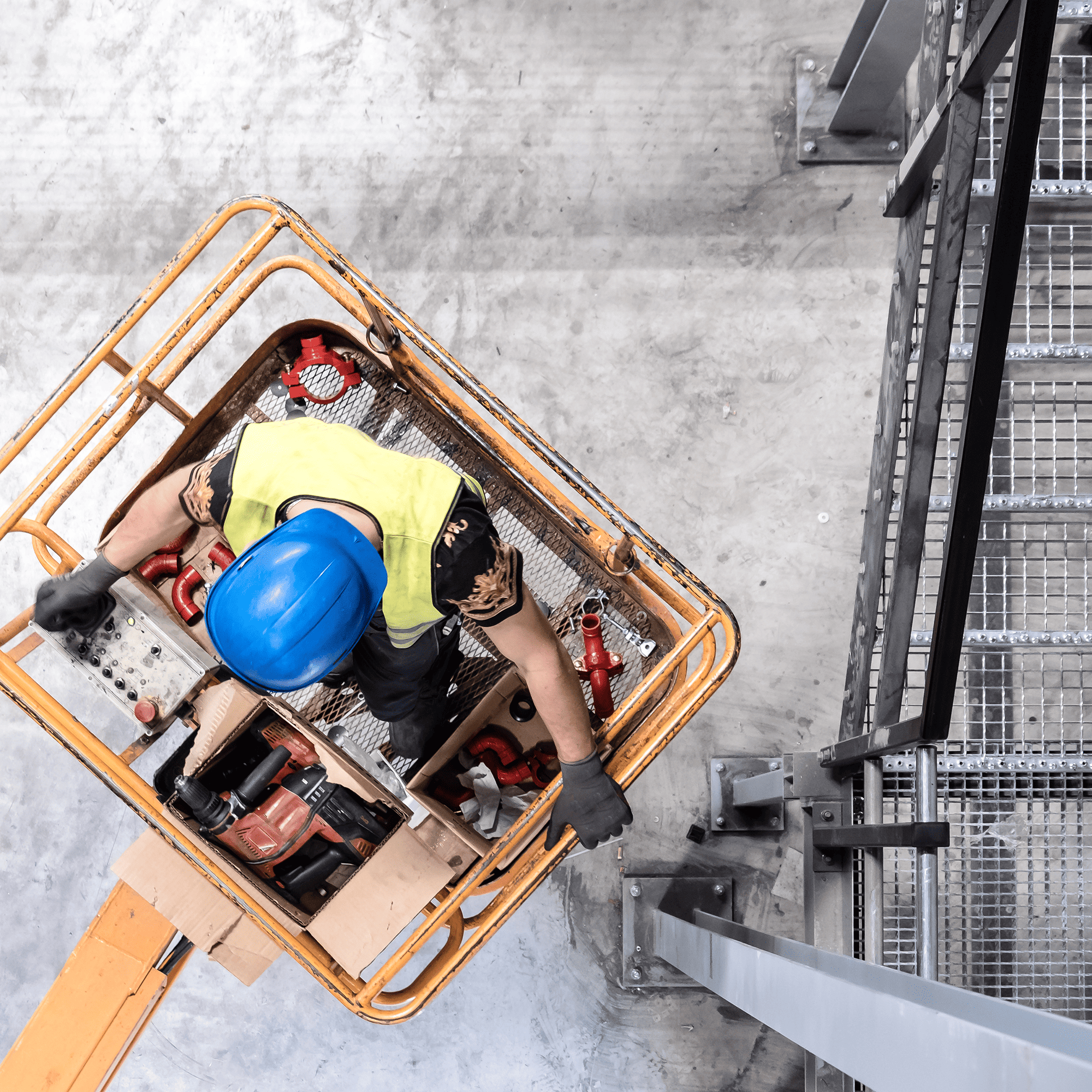 A worker in the basket of an extended boom lift on concrete