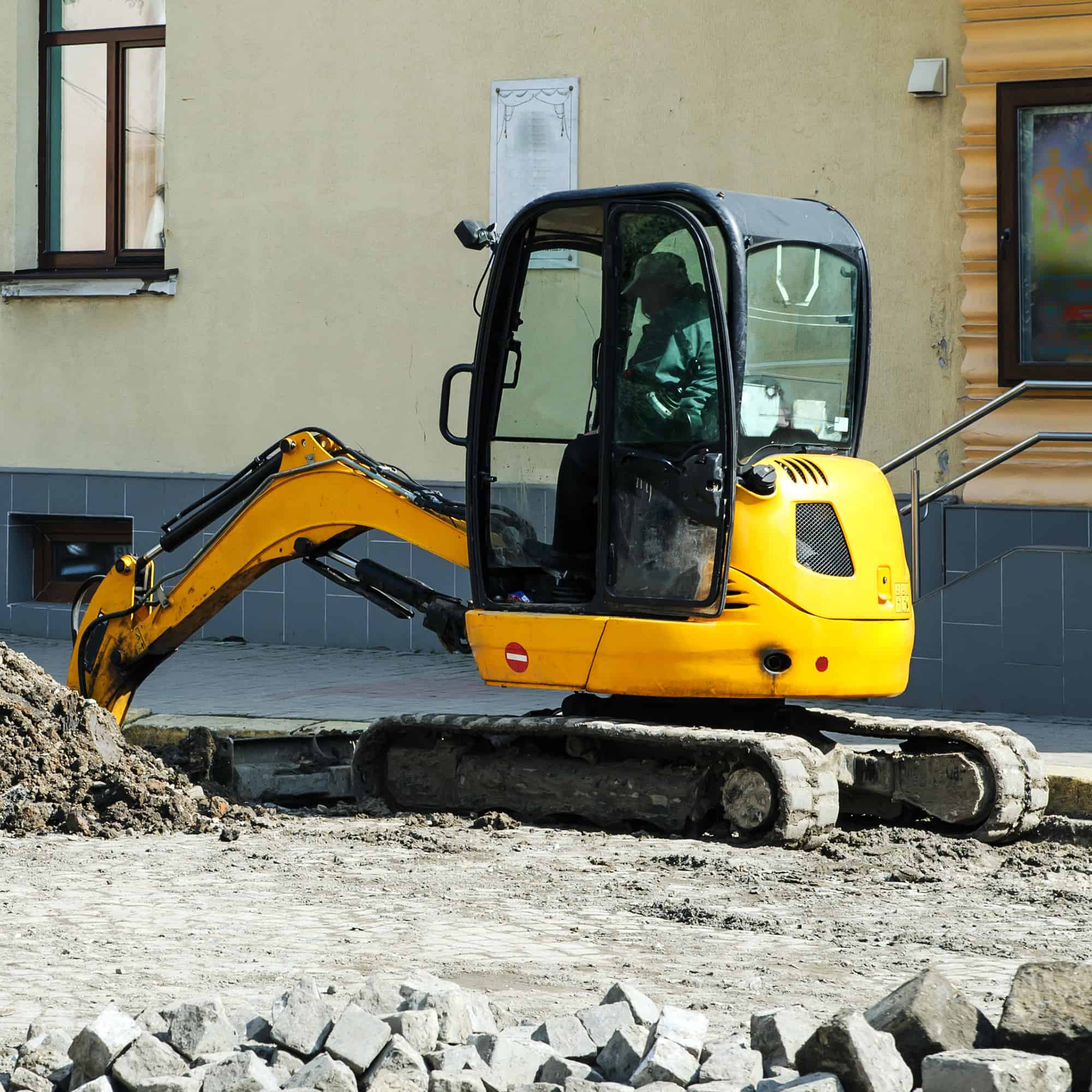 A mini excavator digging a hole next to a building