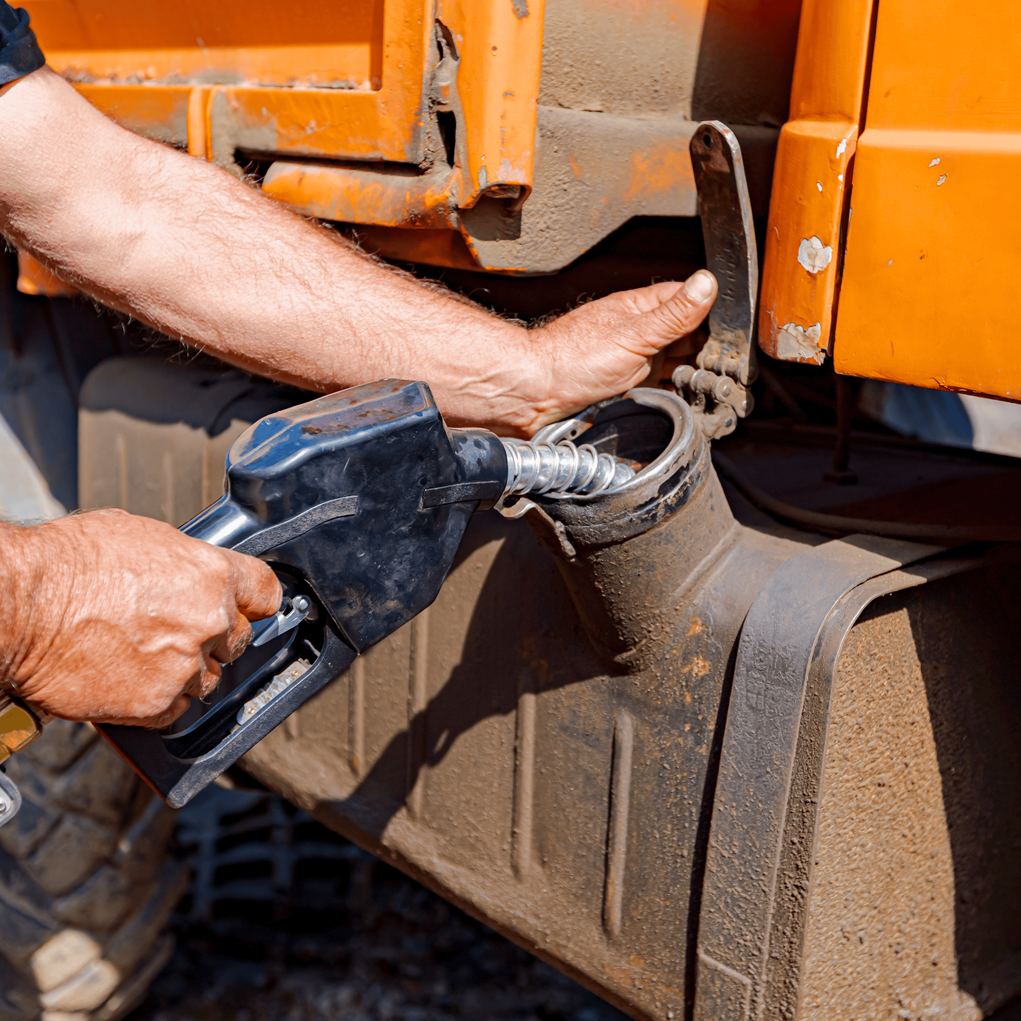 Close up of a pair of hands and a gas pump pumping fuel into a heavy equipment