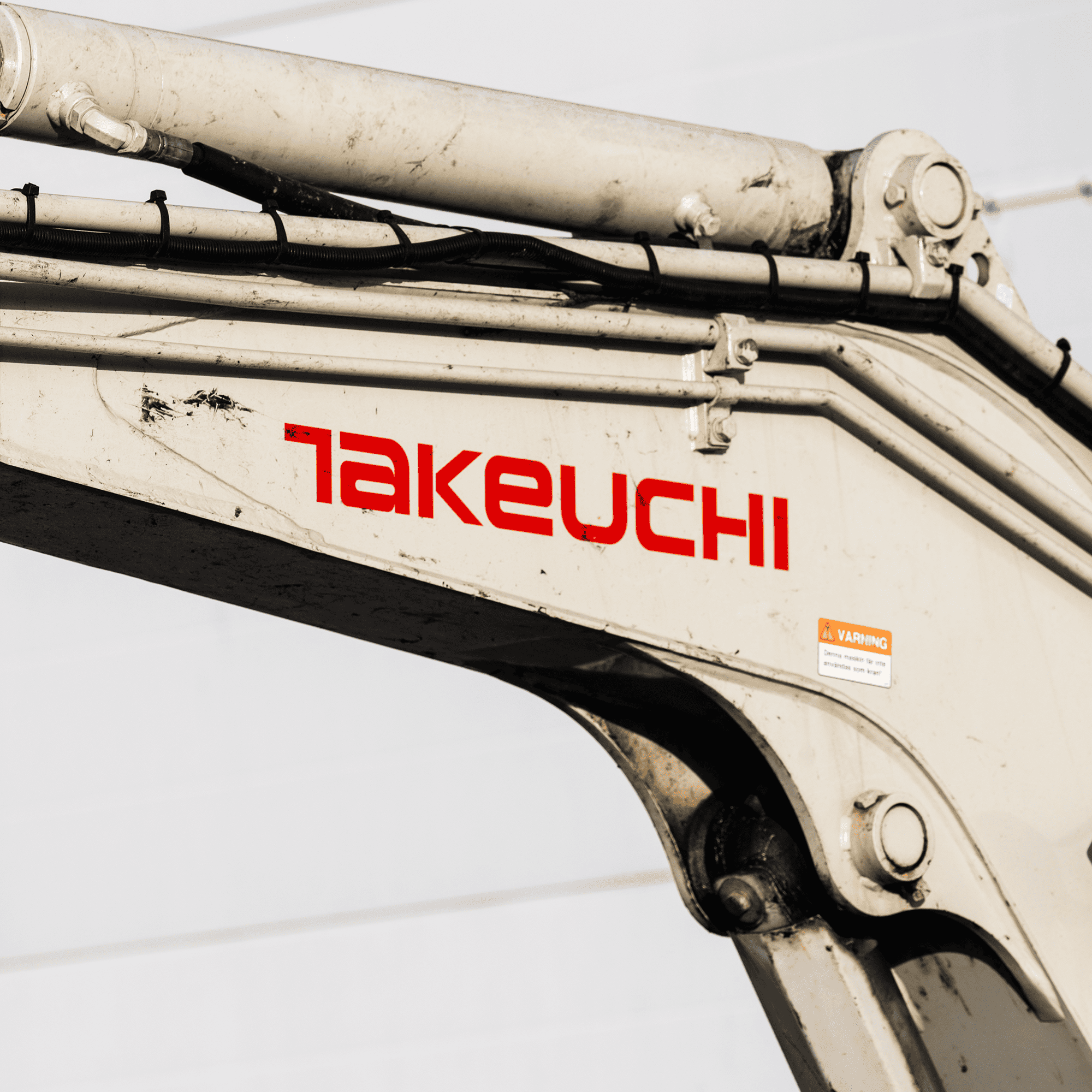 A close up of the red Takeuchi logo on a white heavy machine arm