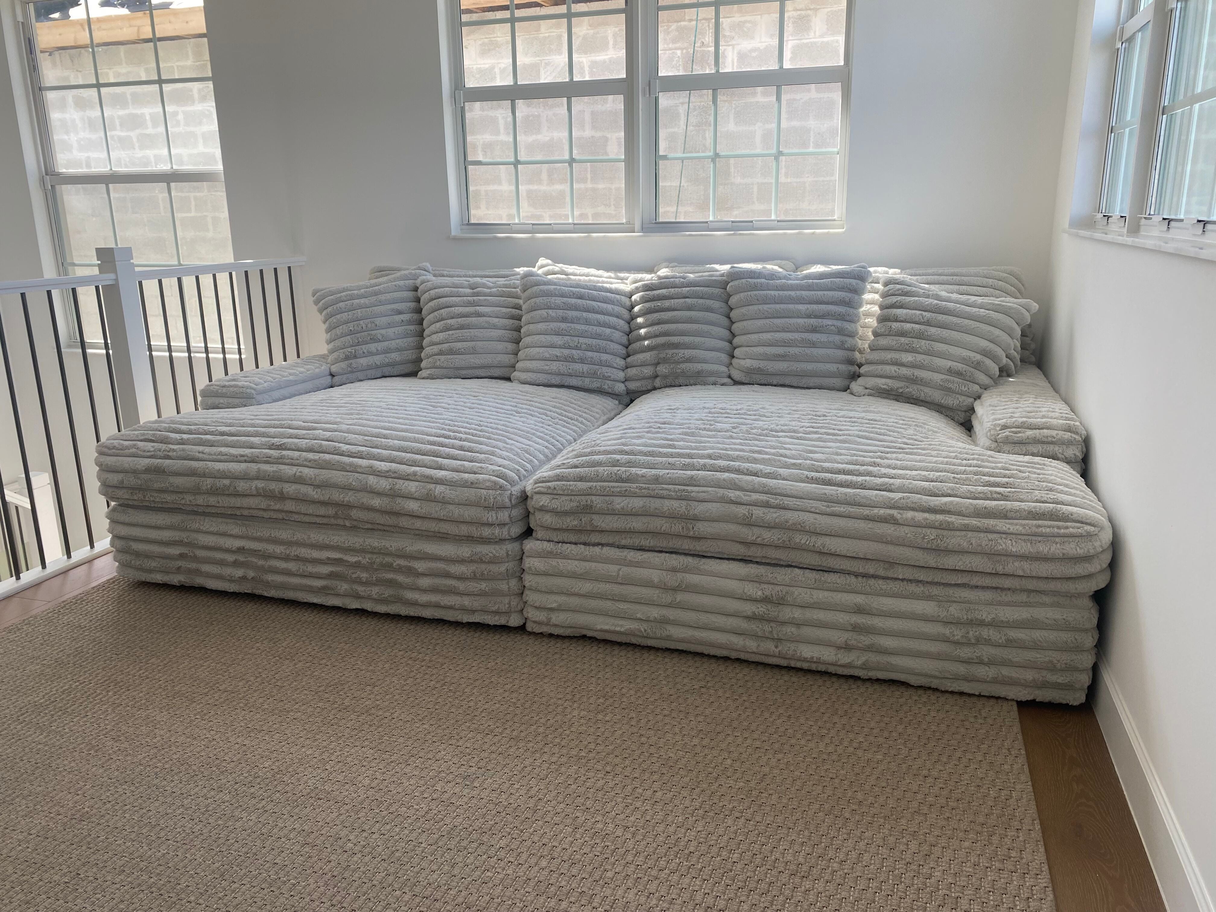 Oversized cushioned sectional sofa in a bright room with large windows.