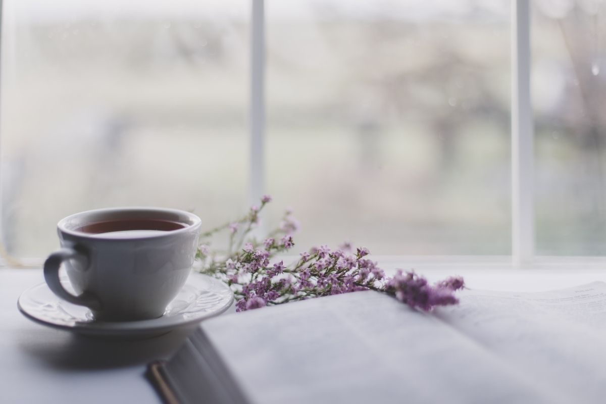 cup of tea in white cup next to book and flowers