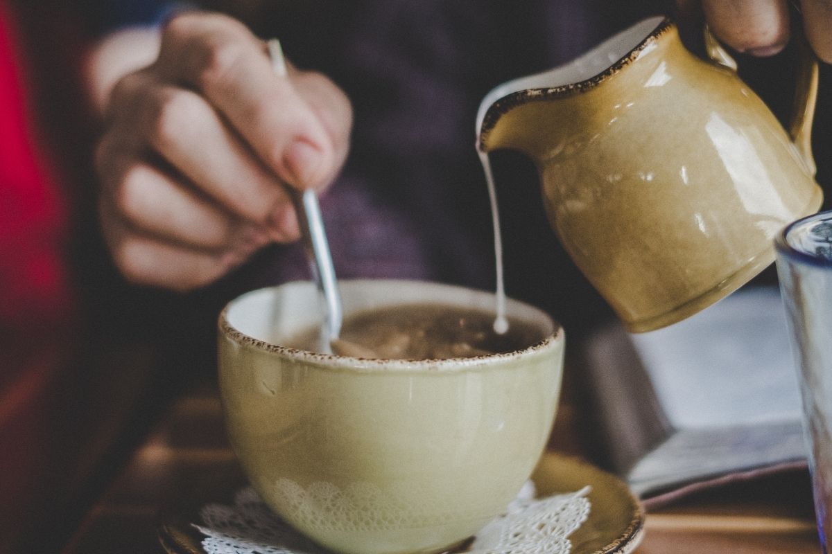 person pouring milk from jug into cup of tea