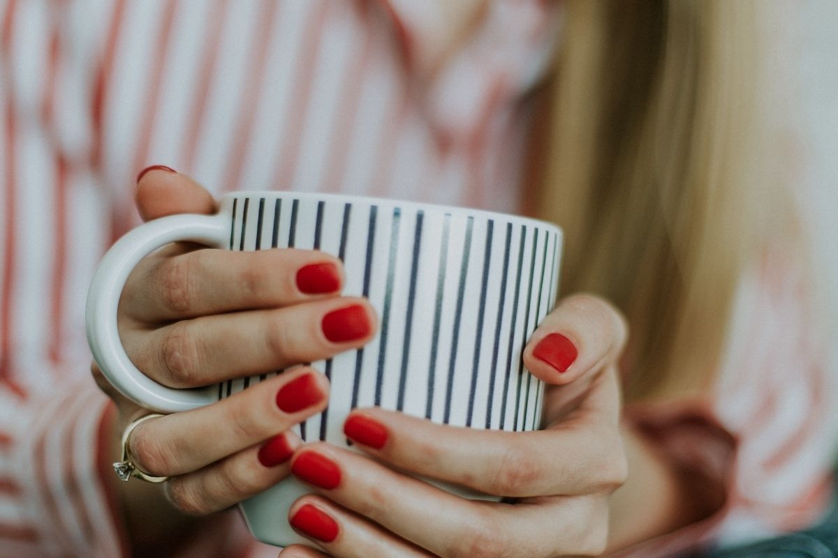 womans hands holding striped cup of tea