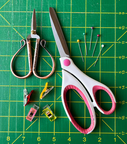 Two pairs of scissors, some sewing clips and pins organized atop a green cutting mat