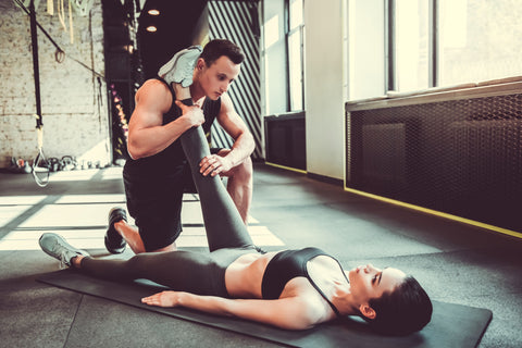 male personal trainer stretching hamstrings of female client laying down