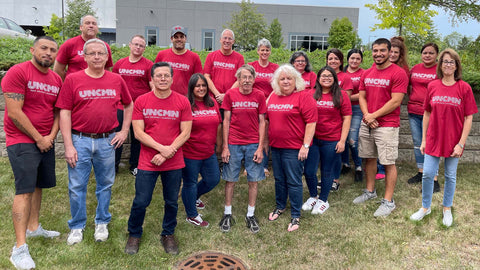 20 of the Uncommon Threads staff standing for a group photo wearing matching red shirts that say "UNCMN New Orleans | Summer 2021"