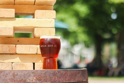 a glass with the words Roscoe Beer Co filled with beer in front of a wood background