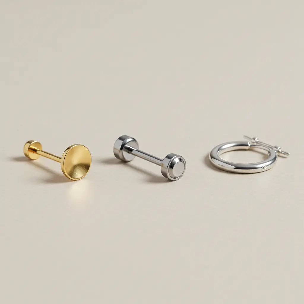 14Kゴールド、インプラント適合チタン、シルバー925の比較フラットレイ。つけっぱなしや敏感肌に配慮した素材選びを質感と色味の違いで分かりやすく提示