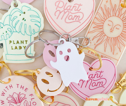 Pile of cute trendy keychains, white ghost on top of pink, yellow, smiley face, acrylic keychains. 