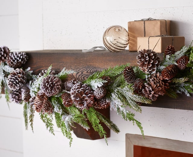 Raz Imports Mantle Garland With Soft Draping Snow Covered Pine and Frosted Pinecones On Natural Wood Mantle