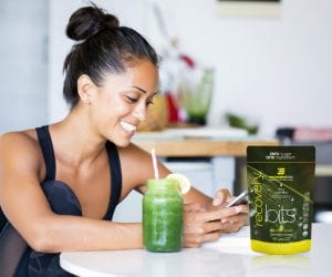 Girl sitting at kitchen table smiling at her phone with a green juice next to her