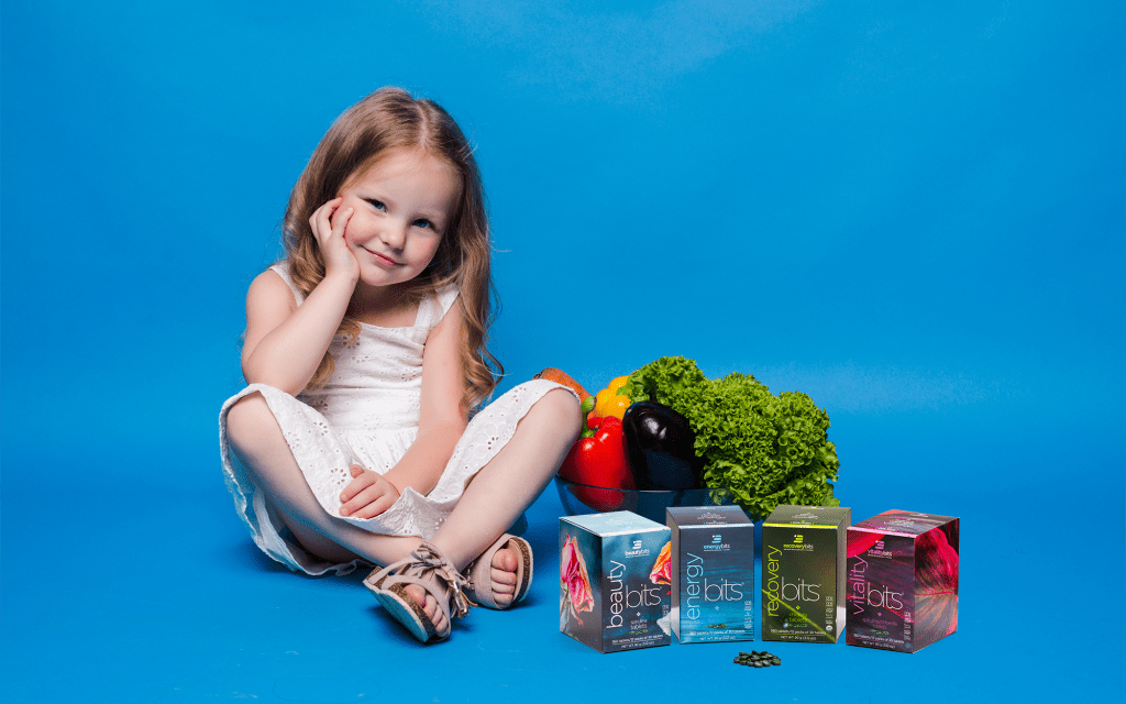 Little girl sitting next to a basket of produce and ENERGYbits mini boxes 